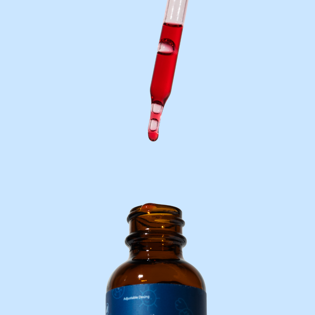 Close-up of a glass dropper filled with red liquid supplement hovering above an open Neupril amber bottle against a light blue background
